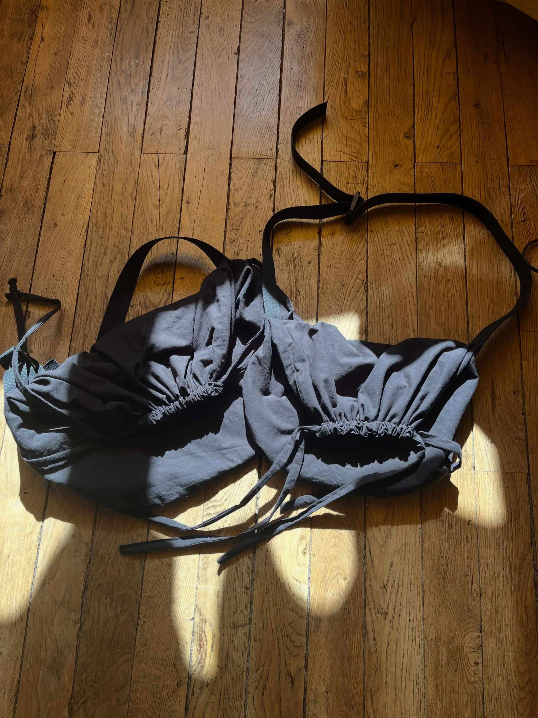 La baluche, sac en tissu gris-bleu à cordons, posée sur le parquet au soleil